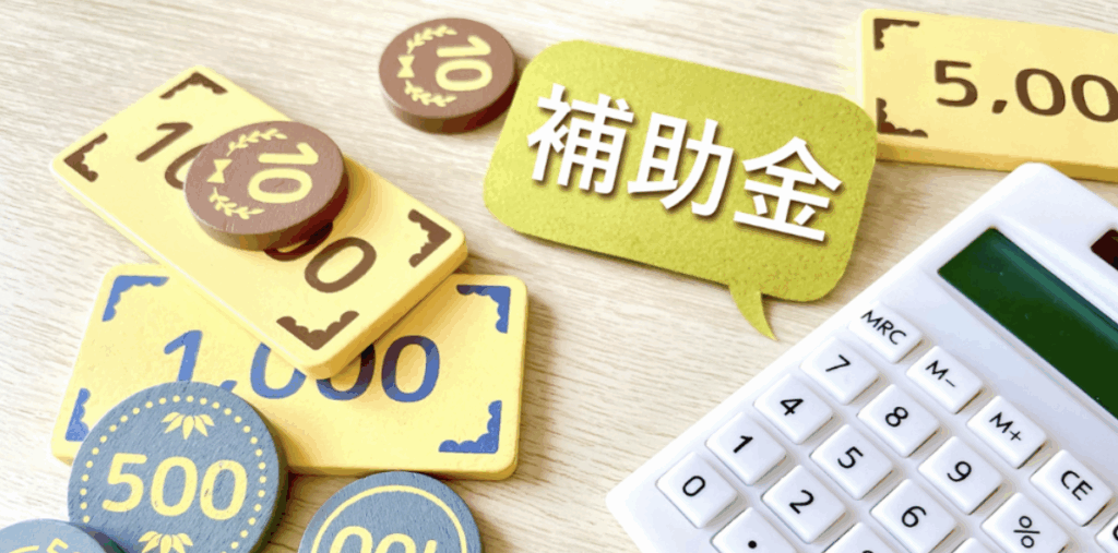 木製コインと紙幣風トークンの横に電卓と吹き出し「補助金」が置かれ、住宅向け補助金の計算イメージを表す写真