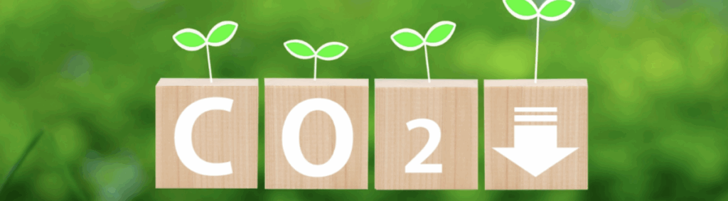 緑背景に芽が伸びる木製ブロック「C」「O」「2」と矢印↓を並べ、CO₂排出削減・環境対策を訴求するビジュアル