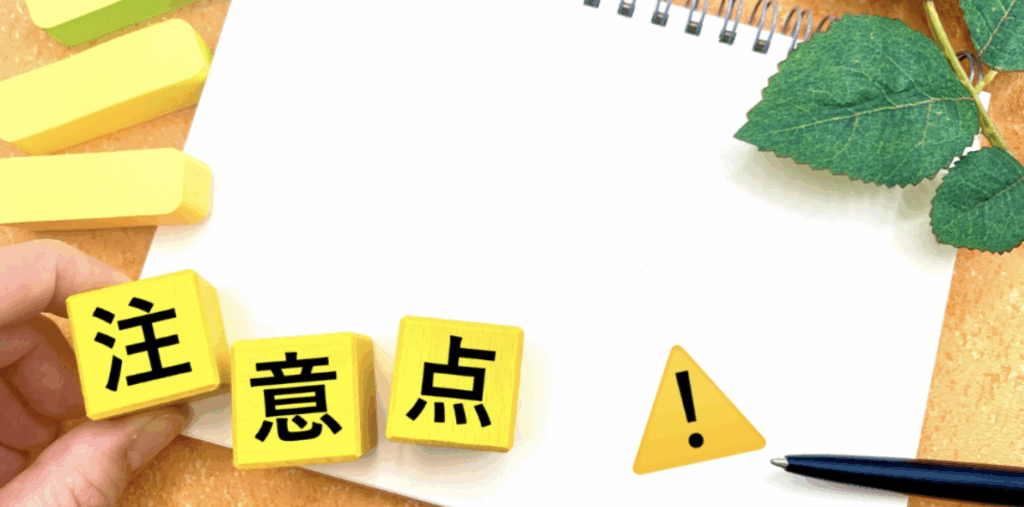 手で並べた黄色ブロック「注」「意」「点」と警告アイコンが、白紙ノート上に置かれた注意事項メモのイメージ
