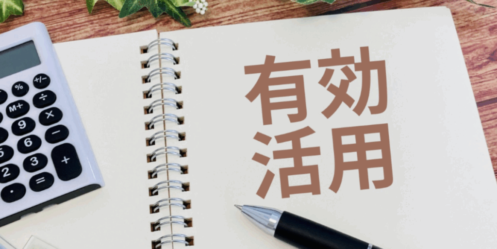 リングノートの空白ページに大きく「有効活用」と書かれ、左に電卓、下にボールペン、周囲に観葉植物を配した資金・土地の有効活用イメージ